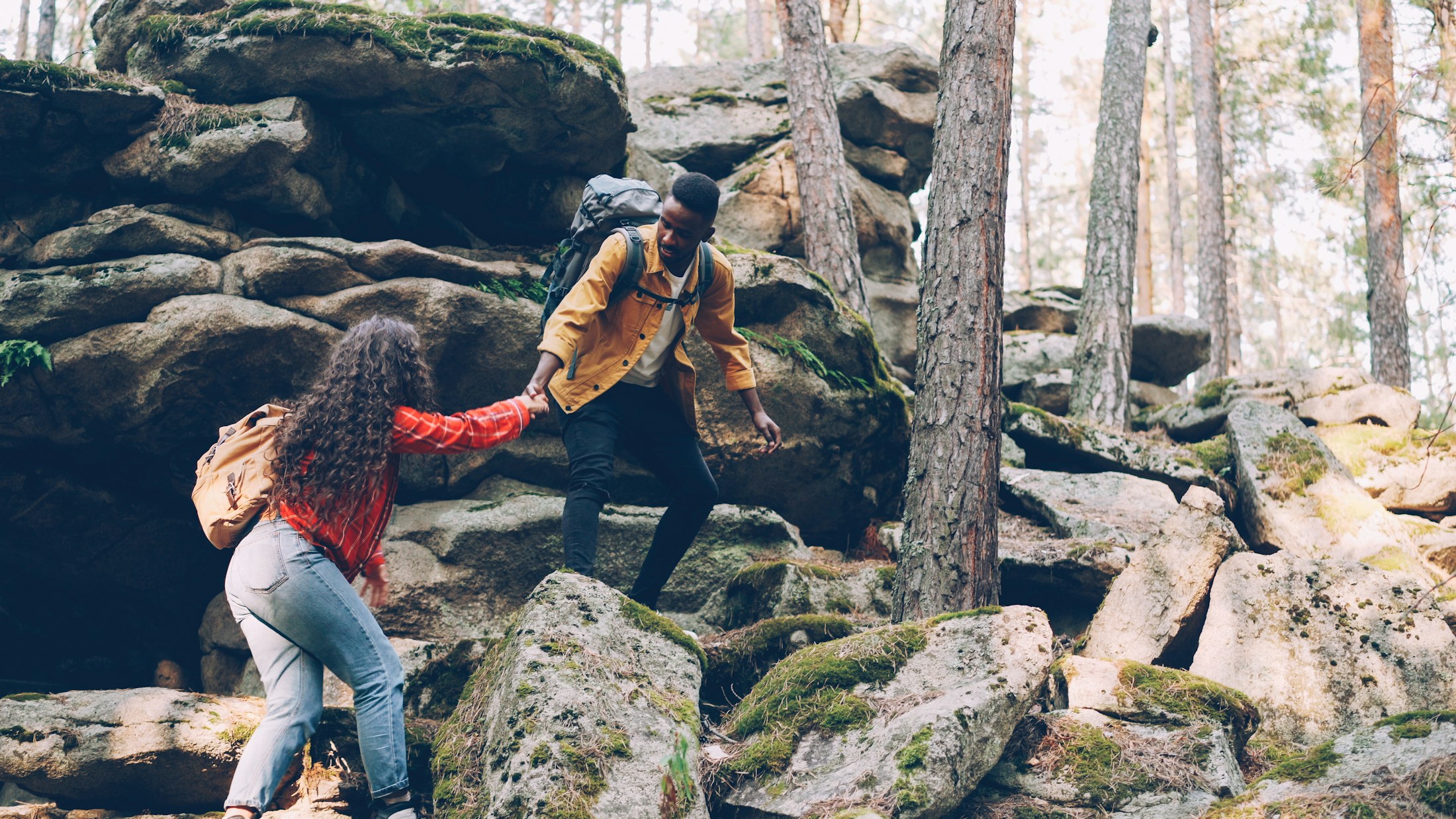 One person helping another climb a rocky trail